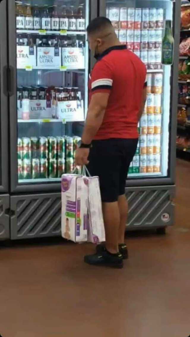 Hombre cargando pañales y mirando triste un refrigerador lleno de cervezas