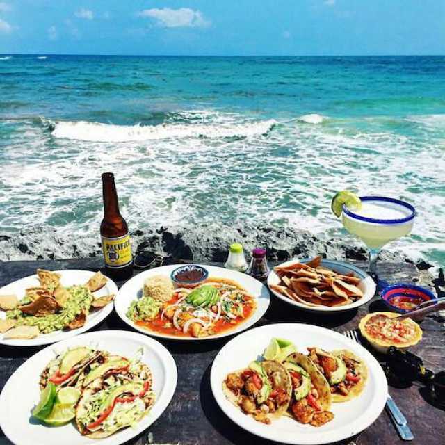Varios platillos de comida y una cerveza frente a la playa